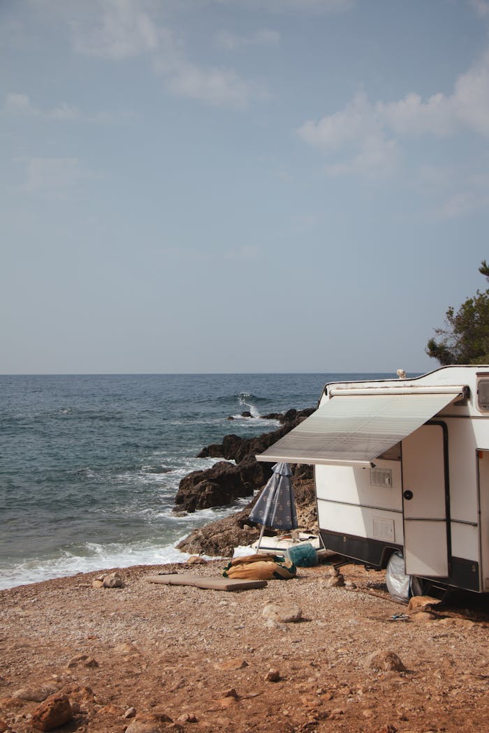 how-we-are Camper parked on rocky coast with awning facing the serene Albanian sea under a clear sky.