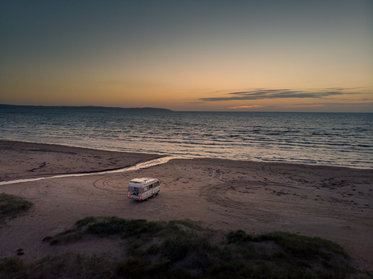 services-01 Camper van parked on the sandy beach of Hallands län, Sweden at sunset with ocean view.
